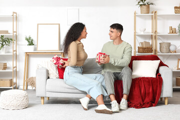 Loving young couple exchanging gifts on sofa at home. Valentine's Day celebration © Pixel-Shot