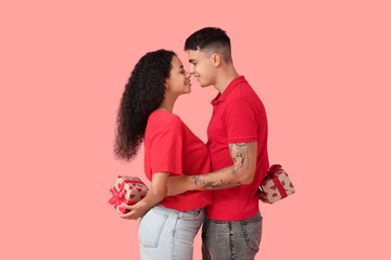 Loving young couple with gift boxes behind their backs hugging on pink background. Valentine's Day celebration