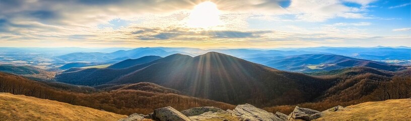 Obraz premium Panoramic view of Carpathian Mountains with sun rays, rolling hills, and majestic peaks under a blue sky.
