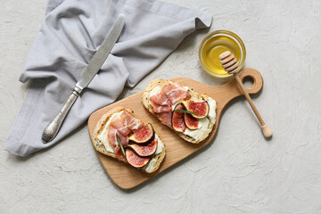 Wooden board of delicious fig bruschetta with prosciutto and ricotta cheese on white background