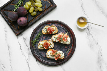 Plate of delicious fig bruschetta with ricotta and blue cheese on white background