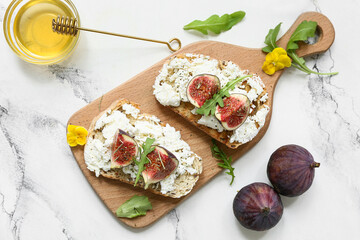 Wooden board of delicious fig bruschetta with ricotta cheese and arugula on white background