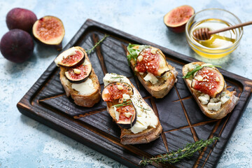 Wooden board of delicious fig bruschetta with different cheese and bowl of honey on blue background, closeup