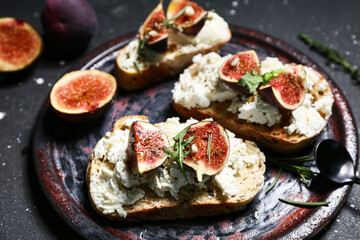 Plate of delicious fig bruschetta with ricotta cheese and arugula on black background, closeup