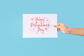 Female hand holding greeting card with text HAPPY VALENTINE'S DAY on blue background