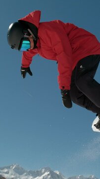 SLOW MOTION CLOSE UP: Extreme snowboarder jumping in big mountain ski resort. Detail of snowboard taking off the kicker in groomed snow park. Snowboarding jump on sunny winter day in snb park