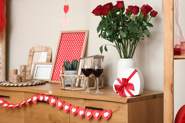 Wooden cabinet with roses, wine, gift box and hearts in festive room. Valentine's Day celebration