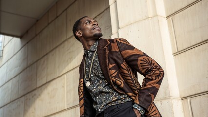 Fototapeta premium Stylish dark-skinned man in patterned jacket against stone wall