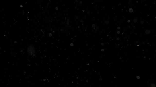 Many dust particles floating in light on empty black background with spotlight from above, close up view.