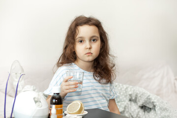 Sick sad little kid girl sits on bed at home and is going to take medication. Flu season. Healthcare concept.