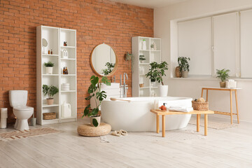 Interior of stylish bathroom with bathtub, houseplants and wooden bench