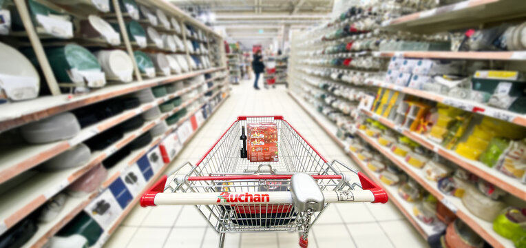 Kosz z produktami, w&oacute;zek sklepowy w supermarkecie, rozmazane tło, wnętrze sklepu, supermarketu, w&oacute;zek na zakupy, p&oacute;łki sklepowe. Hipermarket Auchan. Warszawa, CH Wola Park. Miejsce na tekst