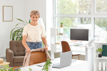 Mature businesswoman hanging her jacket on chair in office