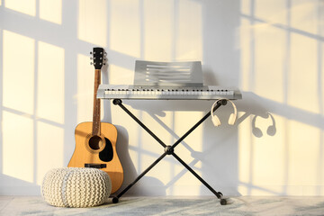Modern synthesizer and guitar near light wall in room © Pixel-Shot