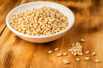 Pine nuts in a white bowl on a wooden table.