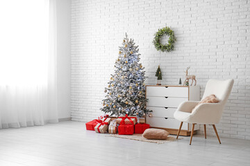 Armchair, chest of drawers and Christmas tree near white brick wall in room