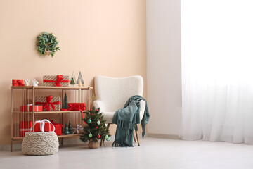 Armchair, shelving unit and small Christmas tree near beige wall in room