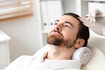 Obraz premium Handsome man receiving injection for hair growth on couch in clinic, closeup