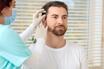 Obraz premium Handsome man receiving injection for hair growth in clinic