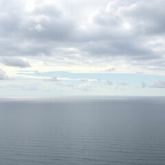 Fototapeta premium A calm blue sea with rolling waves and a distant island silhouetted against a cloudy sky.