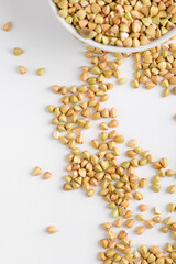 Top view of green buckwheat groats in white plate and scattered on white background