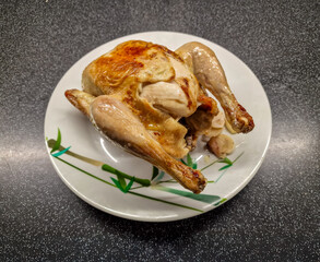 Closeup of a nicely browned and braised chicken, shiny from its own fat on a decorated plate and ready to be cut and distributed to the enthusiast