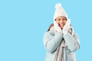 Happy young woman in winter clothes on blue background