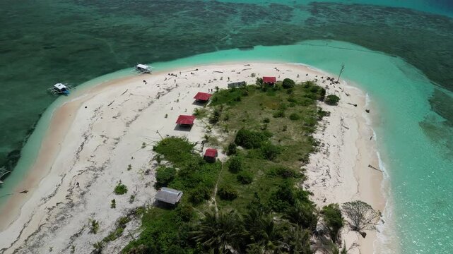 A stunning aerial view of a tropical island in Balabac, Philippines, featuring palm trees, white sandy beaches, and turquoise waters under a bright, partly cloudy sky