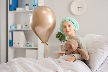 Little girl after chemotherapy with toy bear and golden balloon in clinic. Childhood cancer...