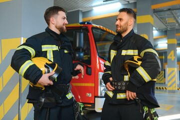 Obraz premium Portrait of two young firemen in uniform standing inside the fire station