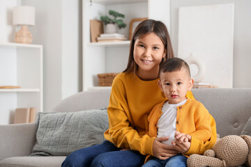 Teenage girl with her little brother hugging on sofa at home