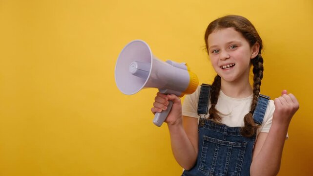 Portrait of excited preteen girl child screaming aside shouting hot news in megaphone, posing isolated over plain yellow background wall in studio. Childhood lifestyle concept