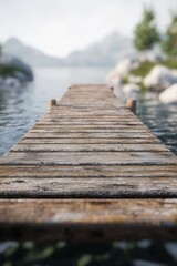 Fototapeta premium Serene wooden pier extending into a tranquil lake surrounded by lush greenery and distant mountains.