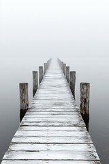 Fototapeta premium A serene wooden pier stretches into the foggy horizon, evoking a sense of mystery and calmness.