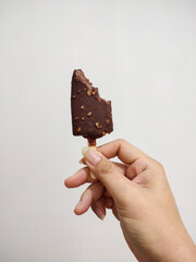 Bitten chocolate peanut ice cream is held in hand on white wall background.