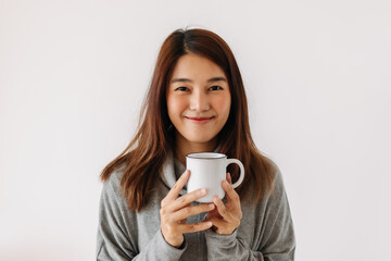 Happy asian woman holding and showing white cup with smiling face in winter, drinking hot drink, isolated over white background wall.
