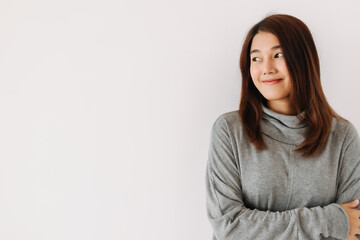 Obraz premium Happy beautiful asian Thai woman wear grey sweater, smiling and looking at empty space while standing isolated over white wall in winter.