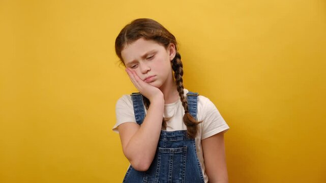Portrait of upset sad preteen girl child put hand on face facepalm epic fail gesture, posing isolated over plain yellow color background wall in studio. Childhood lifestyle concept