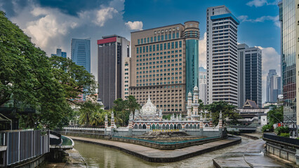 Fototapeta premium The oldest Masjid Sultan Abdul Samad mosque at the confluence of the rivers. Weathered steps, galleries, arches. Domes and spires against the modern city skyscrapers. Blue sky, clouds. Kuala Lumpur.