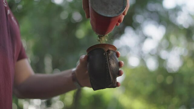 Close-up of a person filling a traditional mate gourd with yerba mate, showcasing the preparation process of this iconic South American beverage.