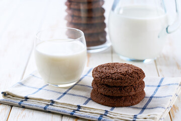 Glass and a jug of fresh milk with chocolate brownie cookies with cracks on a white table, selective focus.