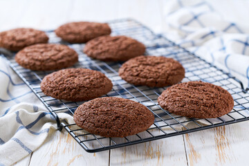 Freshly baked American chocolate cookies cooling on a black wire rack, with in a light kitchen table, selective focus.