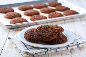 Close up of baking tray with chocolate brownie cookies with cracks on a white table.