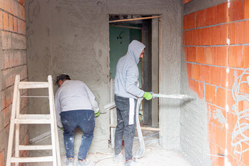Fototapeta premium Plasterer throws plaster on the walls in a new house. A worker hand removes excess plaster with leveler. The process of applying plaster to walls inside a building by machine.