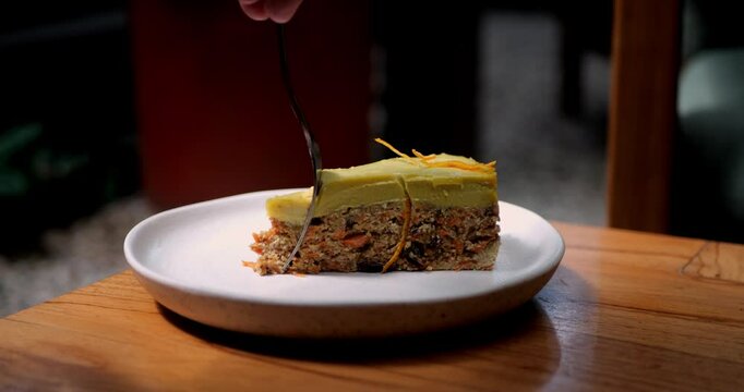 Piece of delicious raw carrot cake with dates and raisins. Topped with mango frosting. Slow-motion video of a piece of vegan carrot cake being eaten with a fork, reverse video.