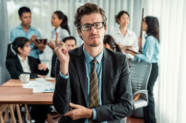 Obraz premium Portrait of happy businessman looking at camera, making finger pointing gesture for advertising product with motion blur background of business people movement in dynamic business meeting. Habiliment