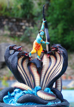 A vibrant sculpture of Lord Krishna subduing the serpent Kaliya, showcasing the divine tale of Krishna dancing on the multi-headed snake, surrounded by dynamic waves and vivid details.


