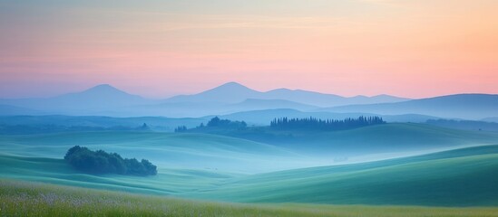 Obraz premium Misty morning sunrise over rolling hills with soft pink and blue tones.