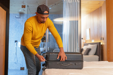 Young man packing a suitcase in a hotel room, getting ready for a departure. Tourism, vacation, and holidays concepts.