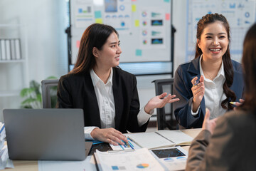 Asian businesswomen discussing charts and data analysis during a meeting, collaborating on project strategy and using a laptop for research